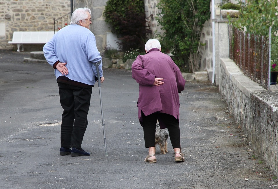 A man and a women walking hunched over, with white hair and canes