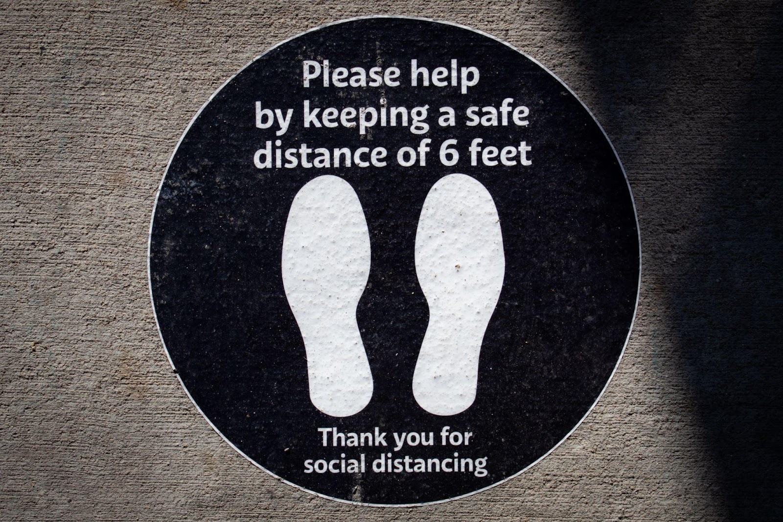 Dos huellas de zapatos en círculo con el mensaje “Por favor ayuda manteniendo una distancia segura de 6 pies. Gracias por el distanciamiento social”.