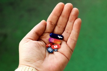 A hand holding pills bearing symbols of various social media apps
