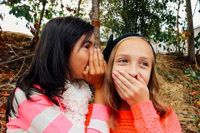 Una chica susurrando un secreto al oído de otra chica.