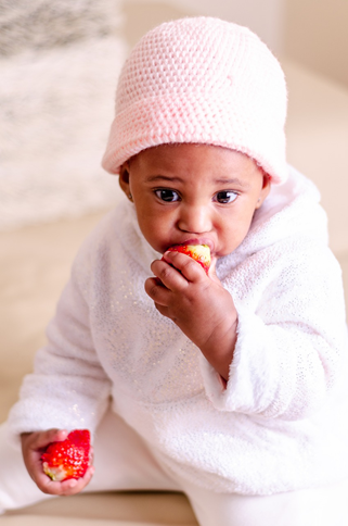 Infant holds two strawberries, eating one.