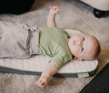 Un bebé explorando el espacio peripersonal recostándose boca arriba y extendiendo sus brazos a ambos lados del cuerpo