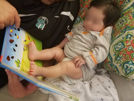 Infant rests both feet on book while caregiver holds it