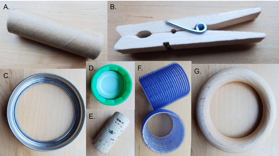 muestra diversos objetos manipuladores: A) tubo de cartón; B) pasador de madera para ropa; C) tapa de tarro de metal; D) tapa de botella de plástico; E) corcho; F) bigudíes de plástico; G) anillo de madera
