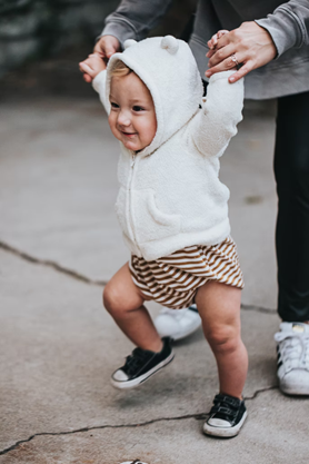 Cuidador que apoya a un bebé sosteniendo a los bebés de las manos sobre la cabeza mientras el bebé practica caminar