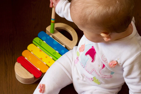 Infant uses a stick to play with a xylophone