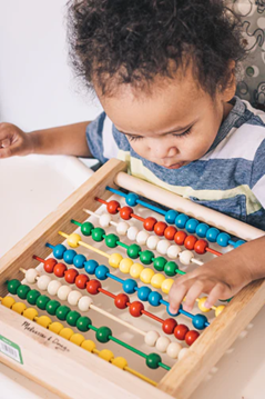 Toddler uses two fingers of left hand to move pieces of an abacus. 