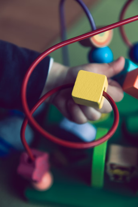 Child reaching through toy with small blocks strung on wires, pausing to examine a yellow block within toy. 