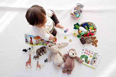 Infantil sentado con diferentes categorías de objetos que los rodean. libros de mesa, figuritas de animales pequeños, peluches y piezas de rompecabezas.