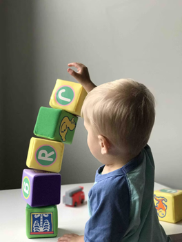 5 small blocks stacked in front of toddler with hand on top and 5th block.