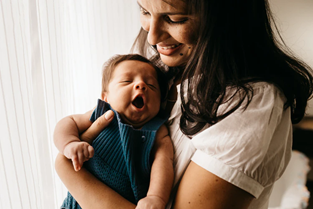 Women caregiver holding yawning young infant in arms as she smiles