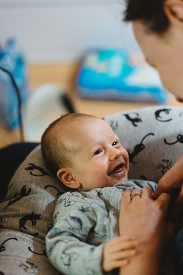Un bebé sonriente mira directamente a los ojos del cuidador mientras el cuidador mira hacia atrás