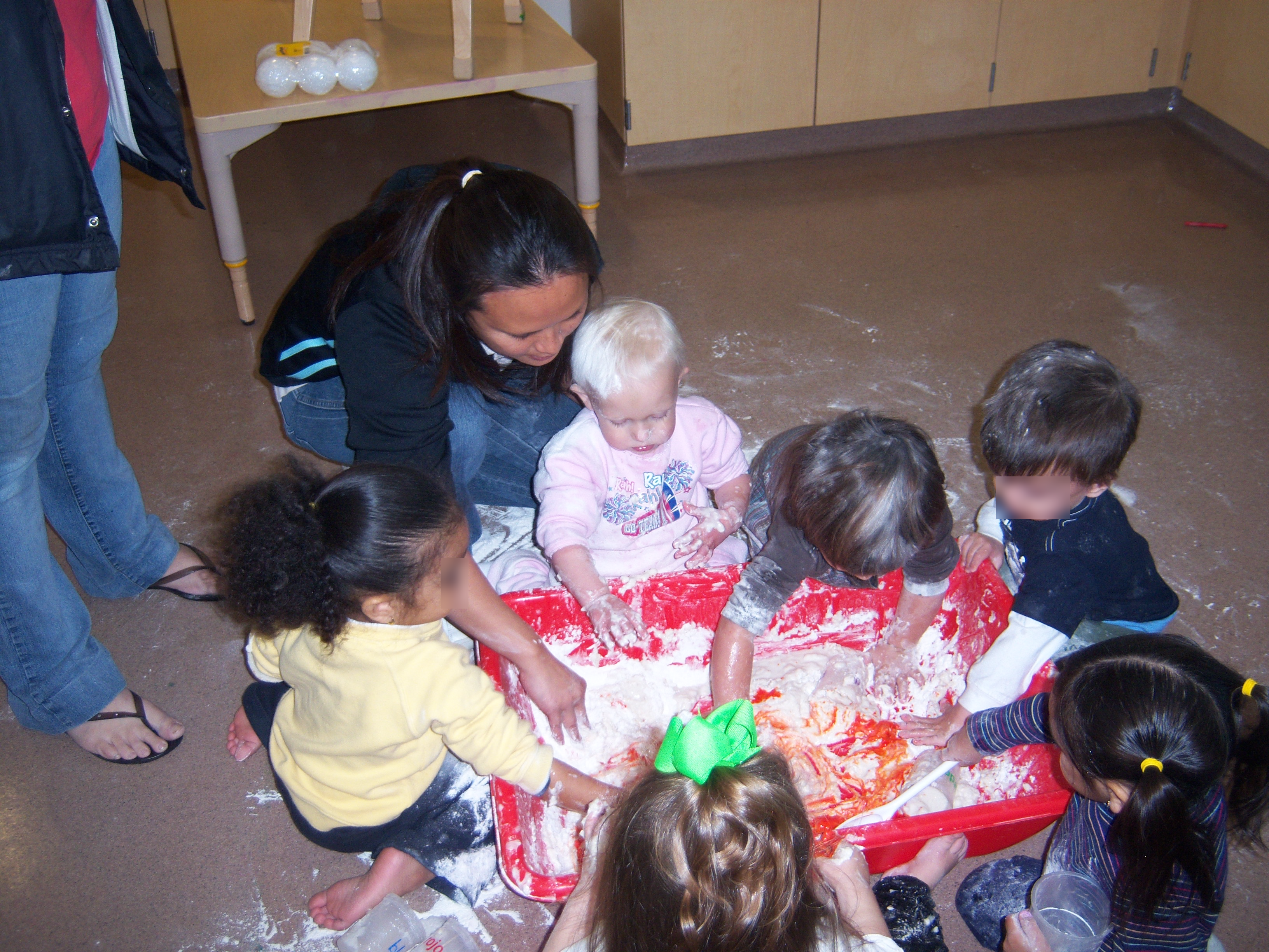 Six Toddlers and caregiver making playdough in large bin