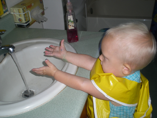 young toddler with hands in sink and water on