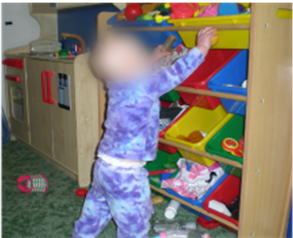 infant standing reaching into open bins on shelves