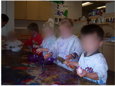 Toddlers stand at low table engaged in activity. 