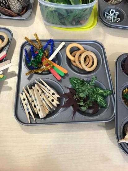 muffin tin with wooden clothes pin, wooden rings, leaves and sparkly pipe cleaners.