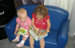 two toddler sit on a child size couch looking at a book