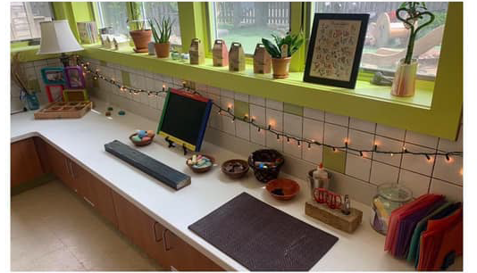 toddler art area with easel, glue, scissors, papers and chalkboard all on low level counter top. 