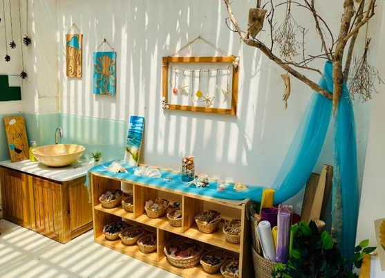 área sensorial para niños pequeños incluye fregadero, dos repisas forradas con cestas abiertas llenas de diversos objetos.