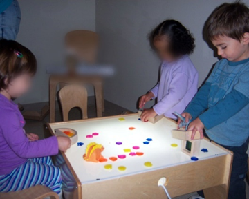 Toddlers at light table with various colored objects on top