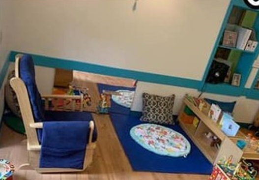 infant environment with rocker, mirror on ground, pillow and blanket on floor with low shelves and a few objects to explore on top. 