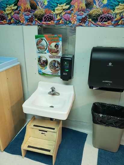 A child sized sink, with step stool, soap and visual representation of hand washing steps. 