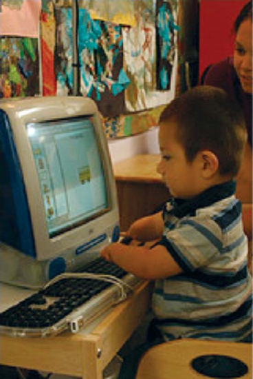 a child with a physical disability uses a computer while a teacher looks on