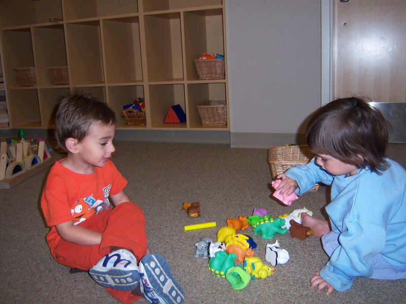 Un niño pequeño ve a otro niño pequeño jugar con pequeños juguetes de dinosaurios