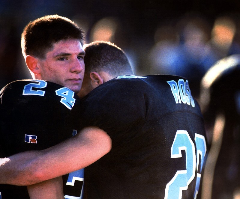 Football players embrace in disappointment after losing a game.