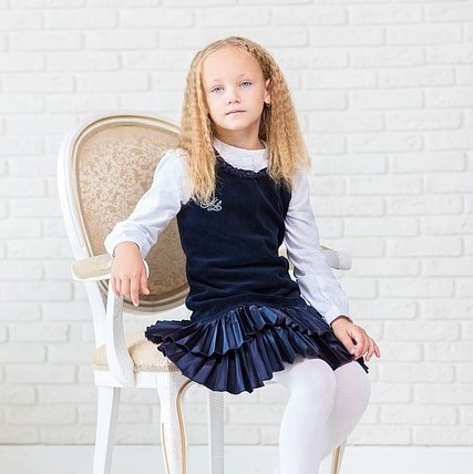 A young girl poses for a portrait in a feminine outfit- tights, pleated velvet skirt, ruffled collar, and tailored cuffs