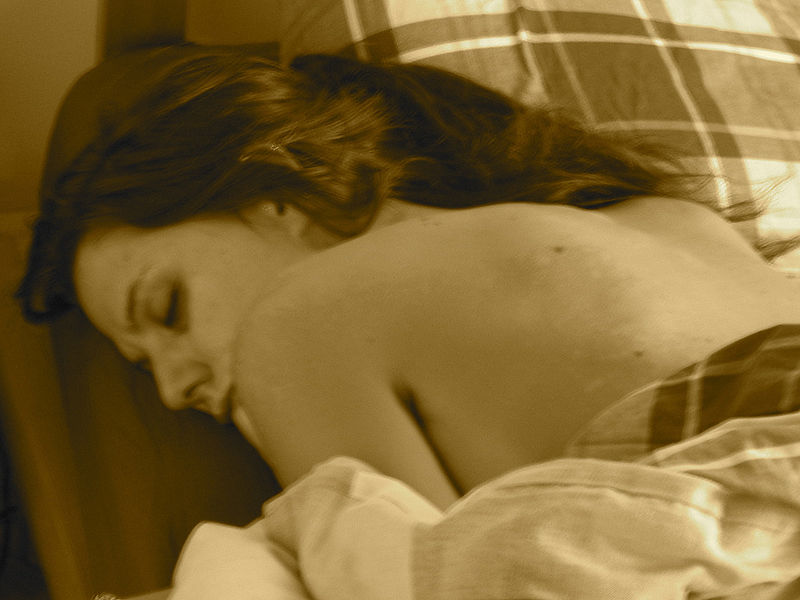 Una mujer de unos 30 años, durmiendo profundamente boca abajo, cabeza sobre la almohada mirando hacia un lado, su largo pelo sobre su espalda desnuda.