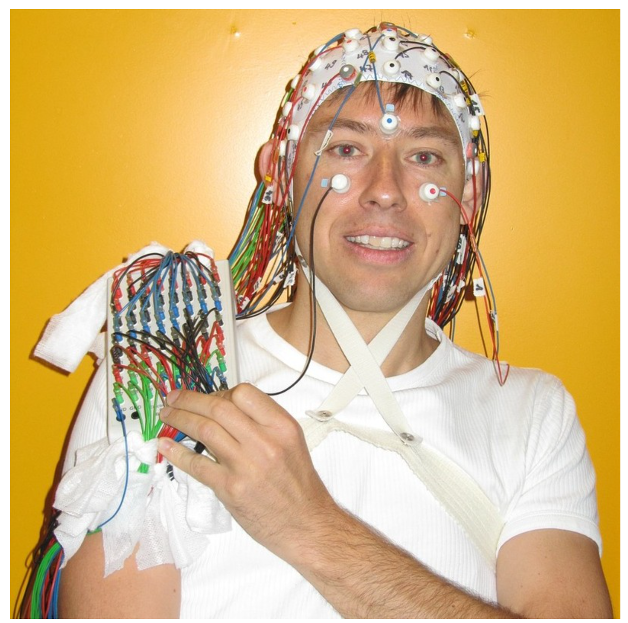 Photo of a young man wearing an EEG cap with abundant wires streaming from the cap covering much of his upper body.