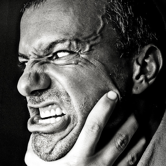 Un hombre con una mirada enfurecida en su rostro y venas abultadas en la frente se tensa contra una mano que lo está asfixiando