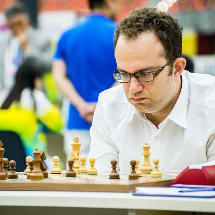 Un hombre se sienta encorvado mirando las piezas en un tablero de ajedrez con una expresión de profunda concentración en su rostro.