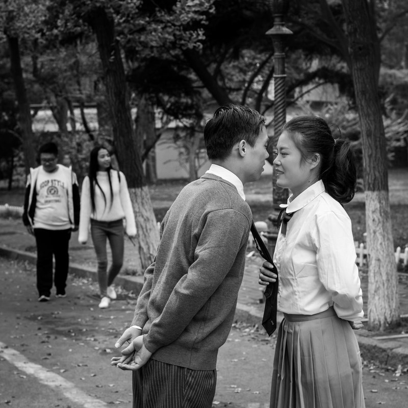Un joven y una mujer vestidos con uniformes escolares están a punto de besarse.