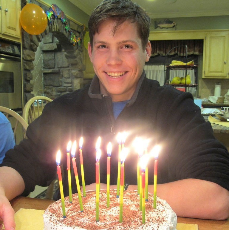 A man smiles as he prepares to blow out the candles on a birthday cake.