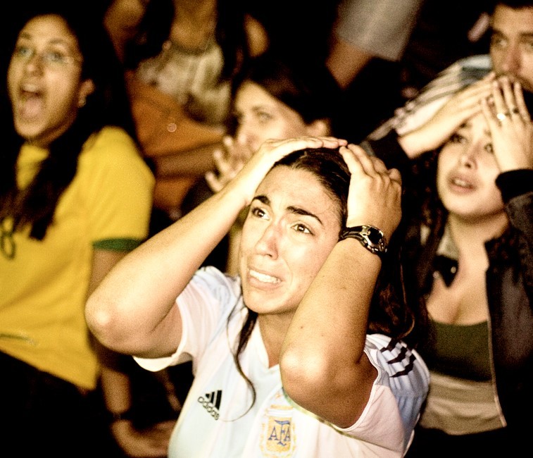 Una fanática del fútbol argentino que lleva una camiseta de la selección nacional reacciona con horror mientras ve un partido en la televisión.
